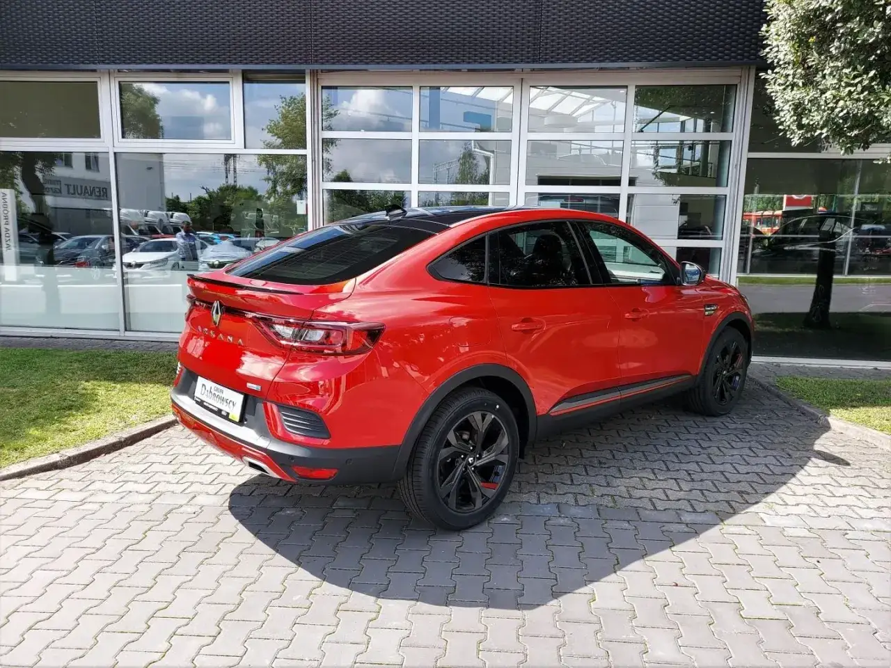 Czerwone Renault Arkana na parkingu przed salonem. Zwróć uwagę na jego sportową sylwetkę i wymiary.