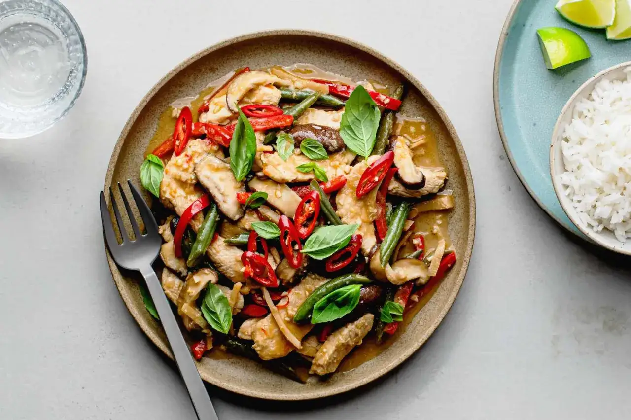 Pyszny kurczak po tajsku z papryczkami chili, fasolką szparagową i grzybami shiitake, udekorowany świeżą bazylią.