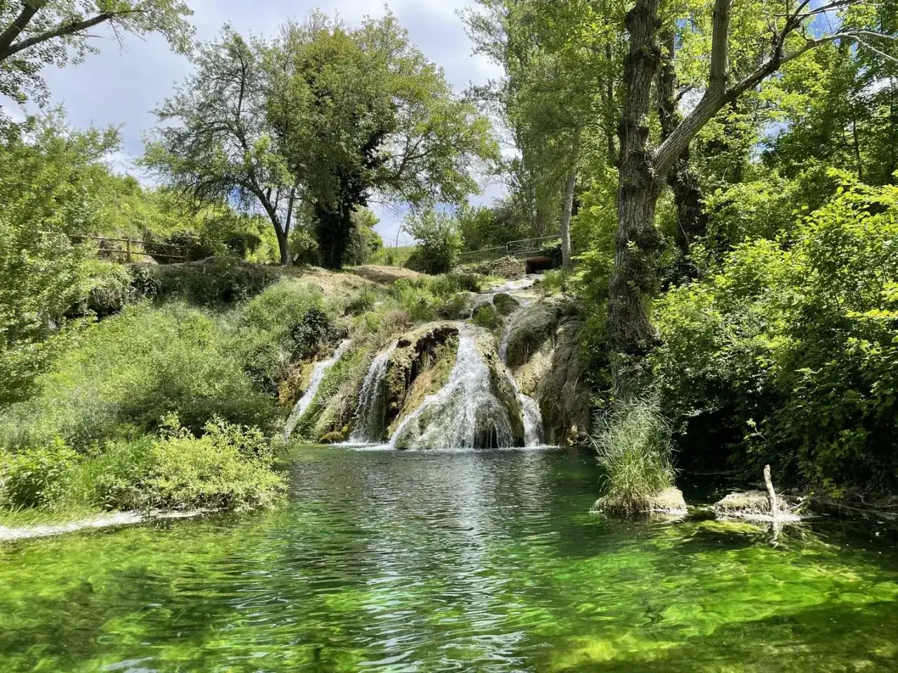 Cascada y poza de agua verde esmeralda, un rinc&oacute;n id&iacute;lico de piscinas naturales en Burgos, rodeado de vegetaci&oacute;n exuberante.