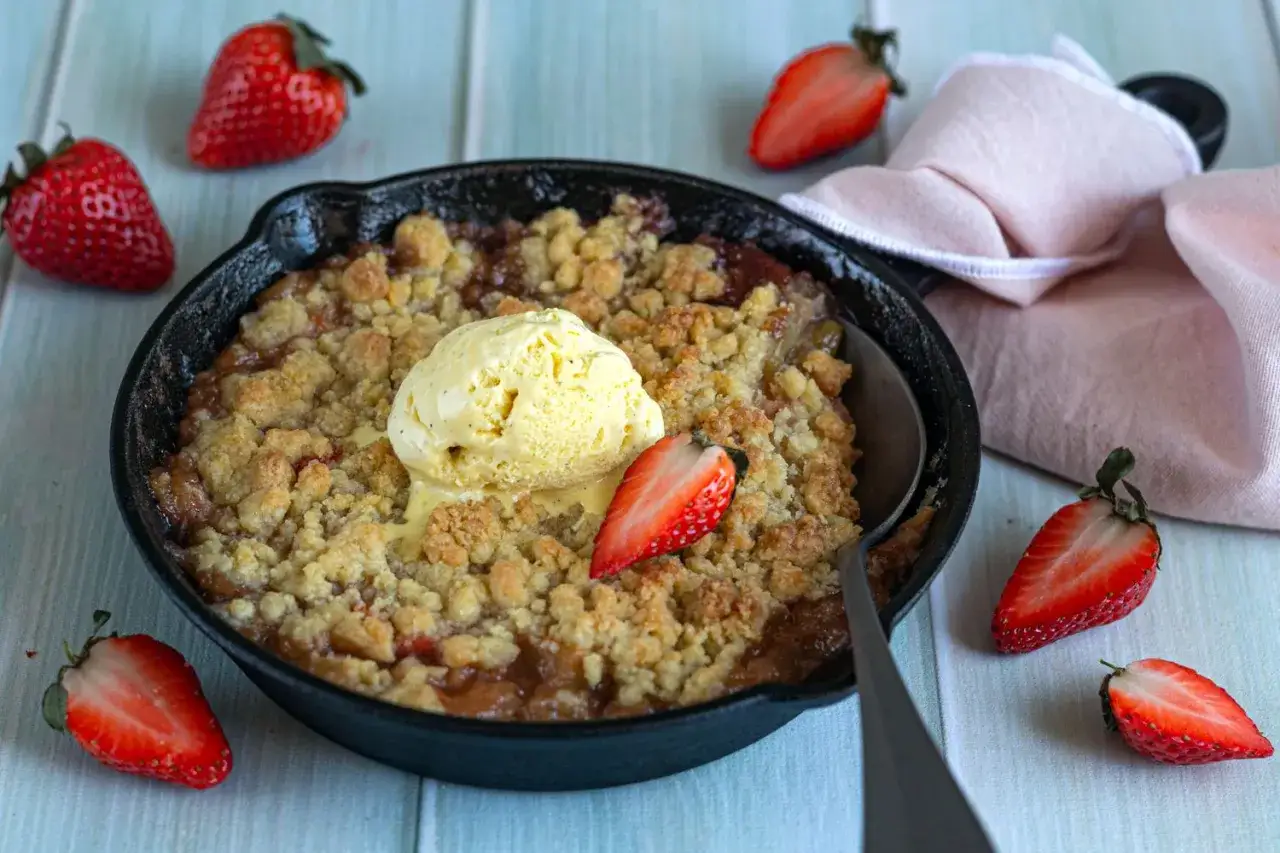 Un d&eacute;licieux crumble rhubarbe fraise, servi chaud dans une po&ecirc;le en fonte, surmont&eacute; d'une boule de glace &agrave; la vanille et d&eacute;cor&eacute; de fraises fra&icirc;ches.