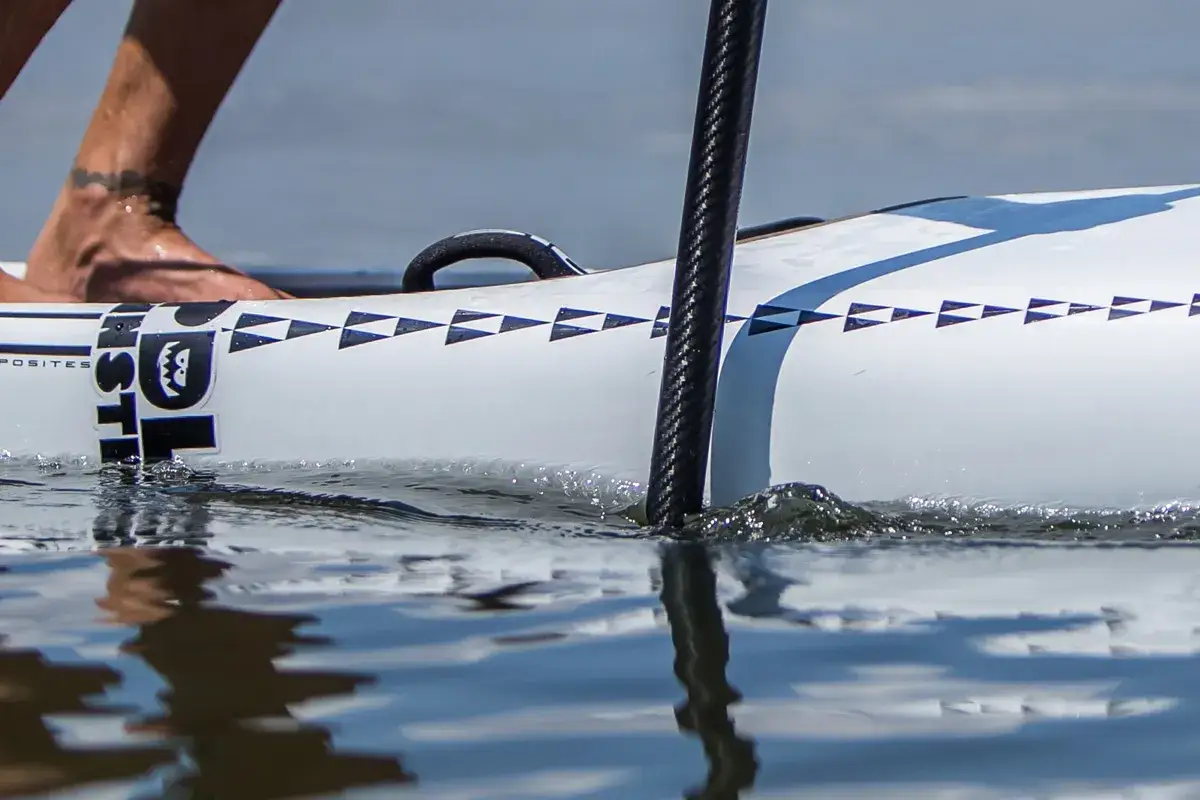 Ein Fuß steht auf einem SUP-Board, während das Paddel ins Wasser taucht. So hält man das sup paddel richtig.