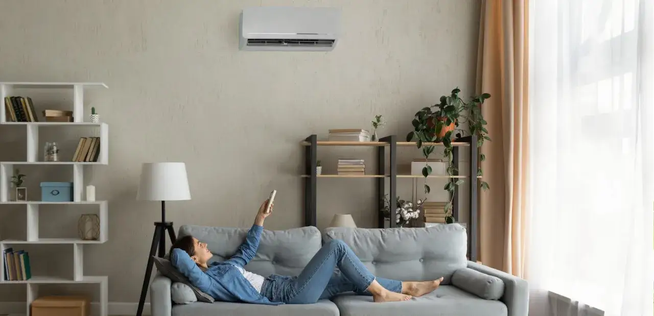 Mujer relajada en el sofá, usando el control remoto para programar el aire acondicionado y disfrutar de la temperatura perfecta.