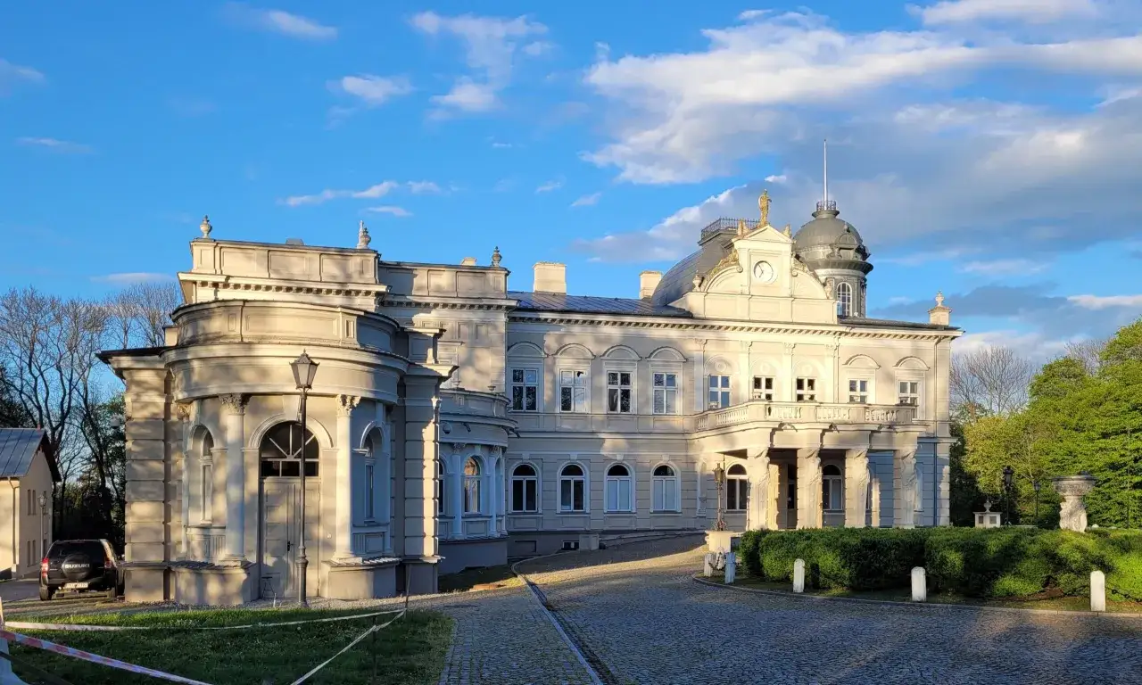 Elegancki pałac w Kościelcu oświetlony zachodzącym słońcem, z charakterystyczną wieżyczką i zegarem.