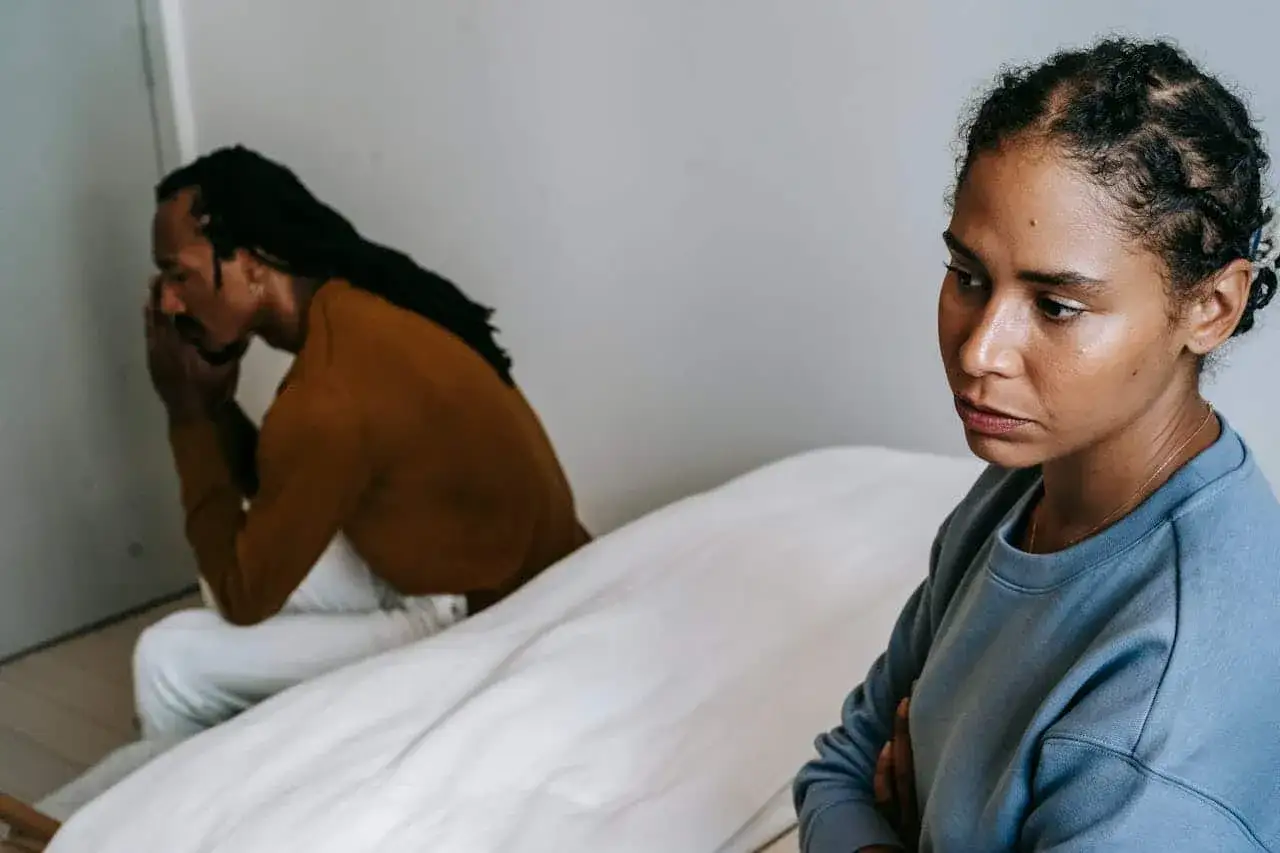 Una mujer mira hacia un lado con los brazos cruzados, mientras su pareja, con la cabeza entre las manos, parece angustiada. Siento que mi pareja me trata con desprecio.
