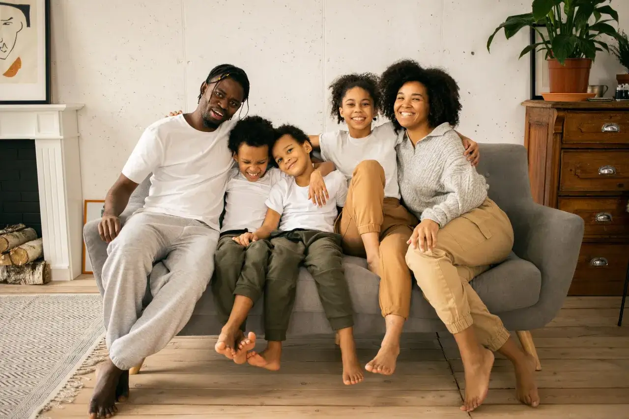 Famille souriante sur un canap&eacute;. Le p&egrave;re, la m&egrave;re et leurs trois enfants profitent d'un moment de complicit&eacute;, loin des soucis de renoncer &agrave; ses droits parentaux et pension alimentaire.
