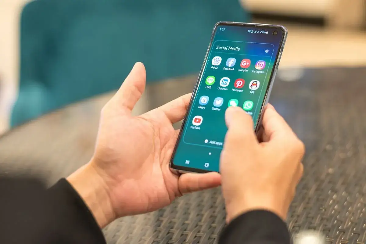 Dłonie trzymają smartfon z ikonami mediów społecznościowych. Użytkownik sprawdza, czy w UK jest roaming, przeglądając aplikacje.