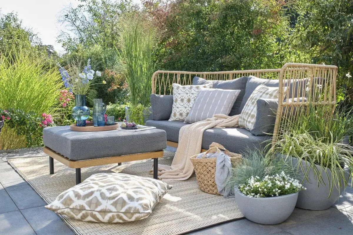 Gemütliche kleine Terrasse gestalten mit Rattan-Sofa, Kissen, Decke und Pflanzen. Einladend und stilvoll.