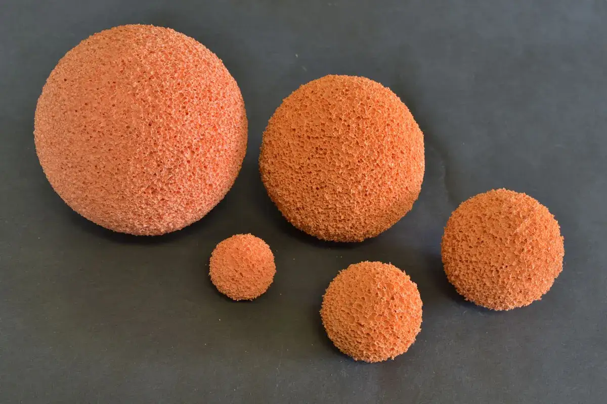 Cinq balles de nettoyage orange, de tailles variées, sont disposées sur un fond sombre.