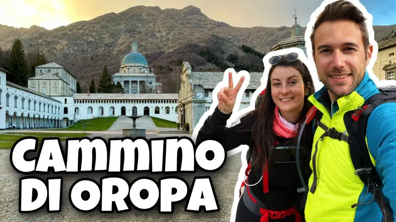 Coppia sorridente in primo piano, sullo sfondo il Santuario di Oropa e le montagne. Inizia il loro cammino di Oropa.