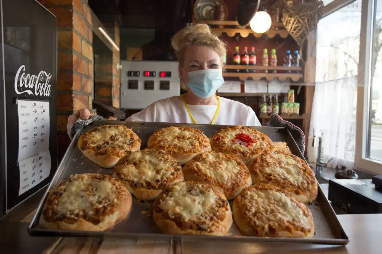 Uśmiechnięta sprzedawczyni w maseczce prezentuje blachę z pizzami. To może być najstarsza pizzeria w Polsce, gdzie tradycja pieczenia pizzy trwa od lat.