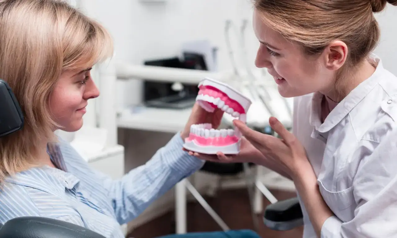 Dentystka pokazuje pacjentce model szczęki, omawiając zabieg założenia plomby.