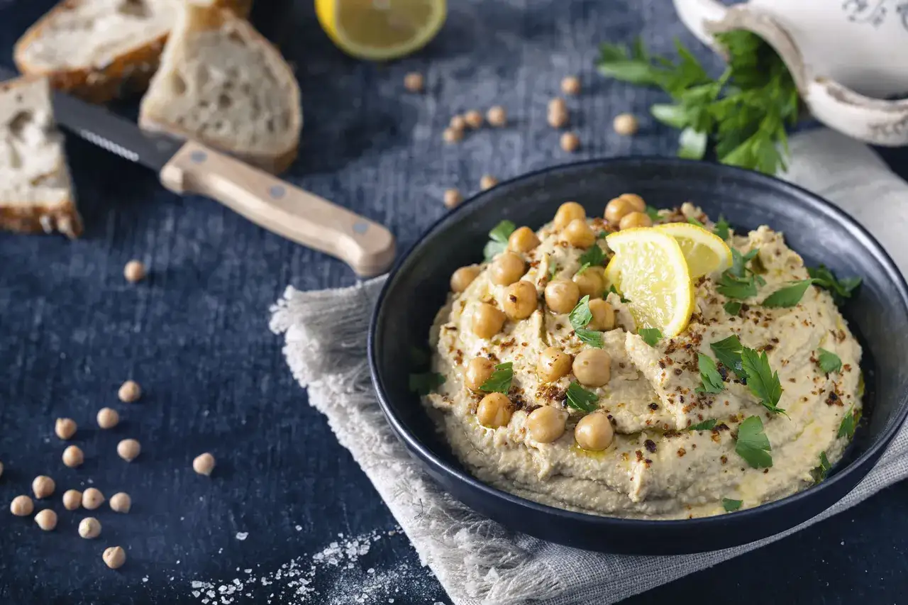 Cremiger Hummus, garniert mit Kichererbsen, Zitrone und Petersilie. Ein köstliches Hummus Rezept Original, bereit zum Dippen mit Brot.