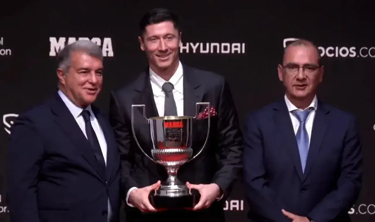 Robert Lewandowski z pucharem Pichichi, obok niego stoją mężczyźni w garniturach.