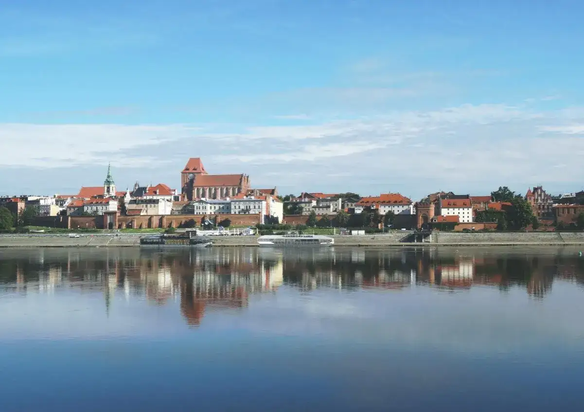 Widok na zabytkowe Stare Miasto Torunia z katedrą i zamkiem, odbijające się w spokojnej Wiśle.