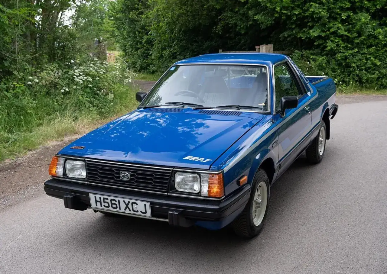 Niebieski Subaru Brat z lat 80. na tle zieleni. Ten kultowy pickup z charakterystycznymi siedzeniami na pace to idealny towarzysz przygód.