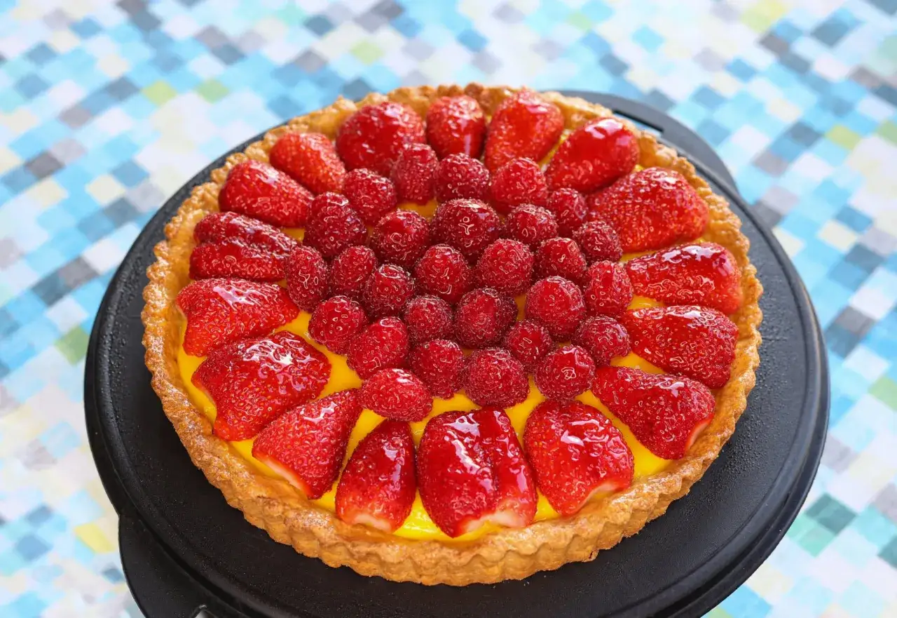 Une d&eacute;licieuse tarte aux fraises et framboises, garnie d'une cr&egrave;me jaune vif, sur un fond color&eacute;.