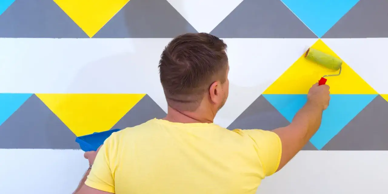 Un homme peint un mur avec un motif géométrique coloré. Une excellente idée motif peinture mur pour un intérieur moderne.
