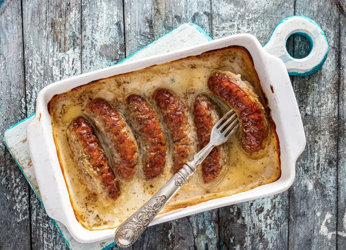 Biała kiełbasa w sosie chrzanowym, zapiekana w naczyniu, z widelcem gotowym do degustacji.