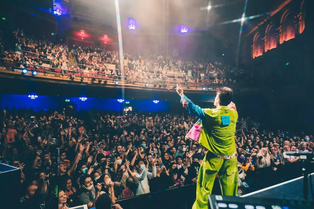 Jacob Collier on stage, facing a cheering crowd. The vibrant Jacob Collier setlist is about to unfold as he gestures to the enthusiastic audience.
