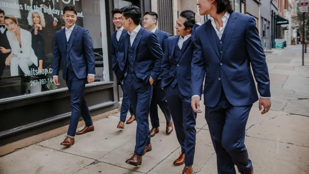 A group of groomsmen in matching navy blue suits walk down a city street, their suits a deep, rich hue.