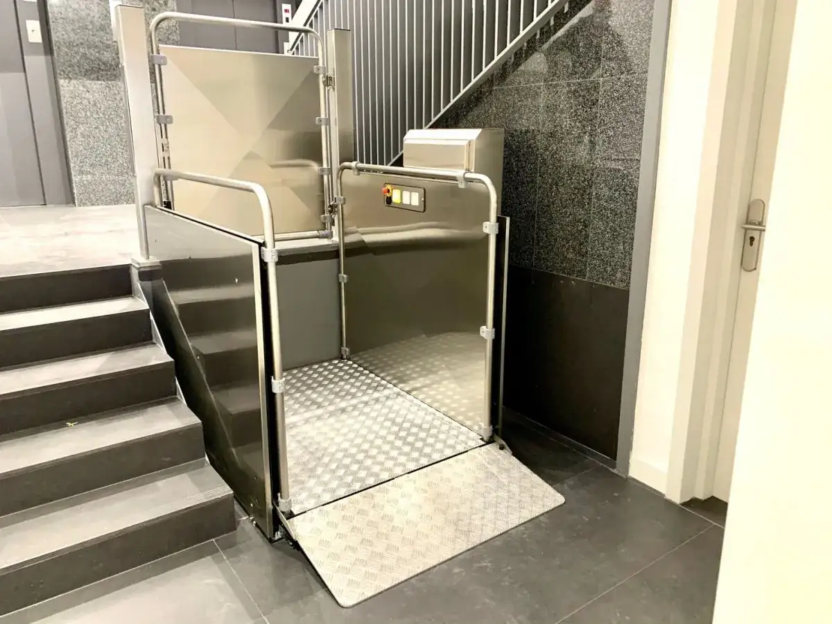 Piattaforma elevatrice per interni in acciaio inox, con rampa d'accesso, installata accanto a una scala.