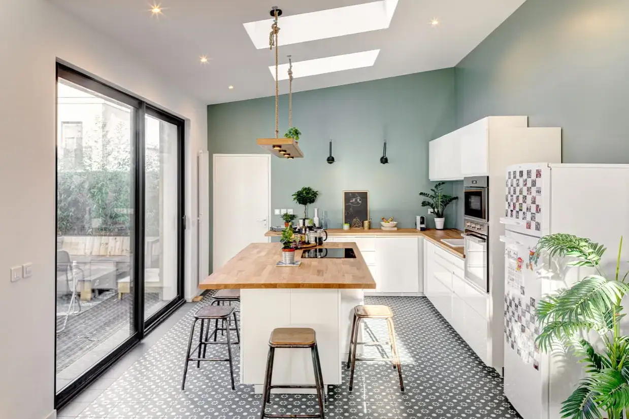Cuisine moderne aux murs vert d'eau et plan de travail en bois. L'îlot central en bois massif invite à la convivialité.