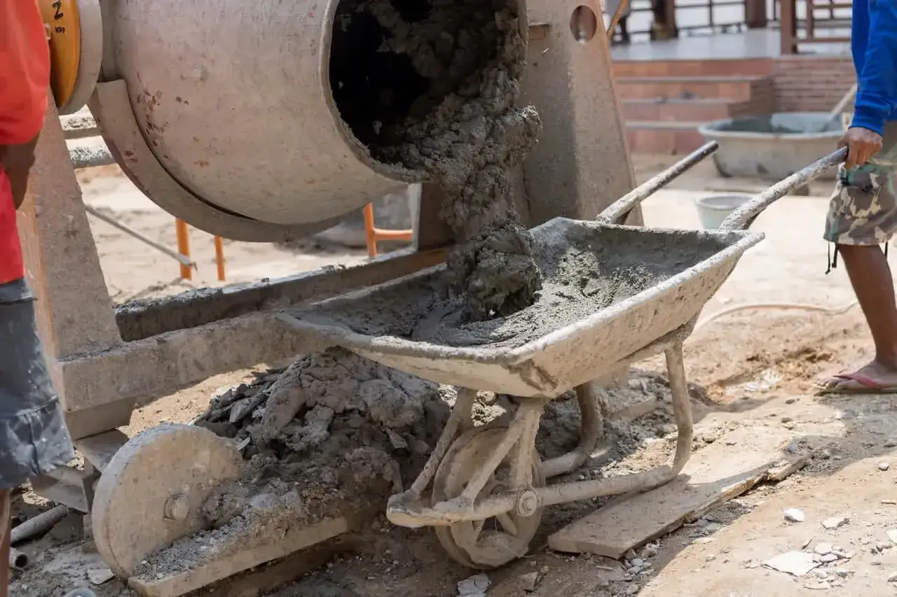 La betoniera scarica cemento fresco in una carriola. Un operaio in maglietta blu osserva, mostrando come fare il cemento per una costruzione.