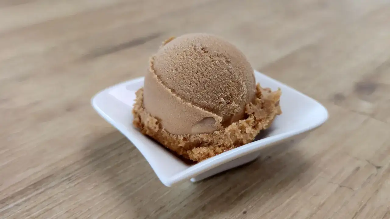 Eine Kugel cremiges Coca Cola Eis in einer weißen Schale auf Holzhintergrund.