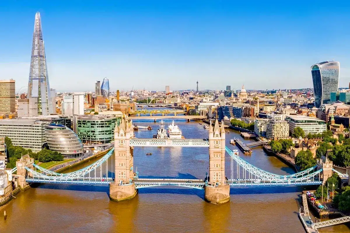 Ein sonniger Tag in London im Sommer. Der Tower Bridge überragt die Themse, während im Hintergrund moderne Wolkenkratzer und historische Gebäude aufragen.