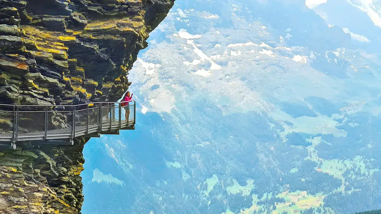 En person njuter av utsikten från en gångbro längs en klippvägg, en fantastisk upplevelse att vandra i Schweiz.