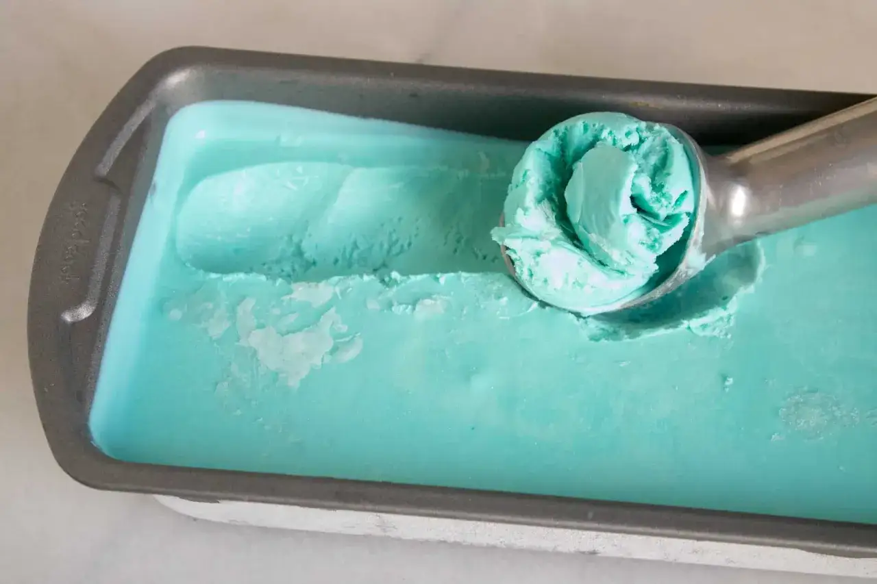 Ein L&ouml;ffel entnimmt eine Kugel hellblaues Schlumpfeis aus einer Metallform. Perfekt f&uuml;r ein erfrischendes Schlumpfeis Rezept!