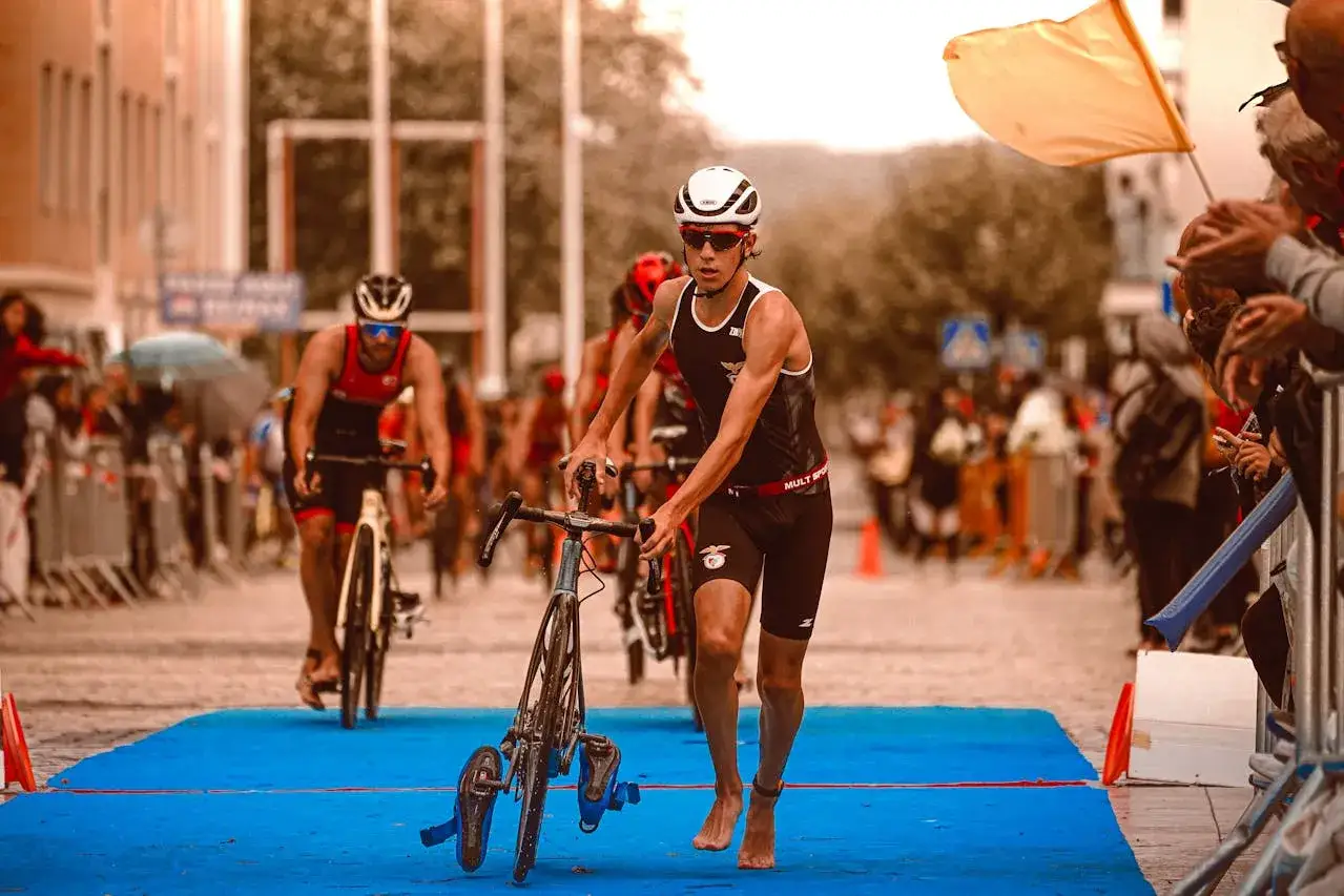 Un athl&egrave;te en plein sprint triathlon, pieds nus, pousse son v&eacute;lo sur la ligne d'arriv&eacute;e sous les encouragements de la foule.