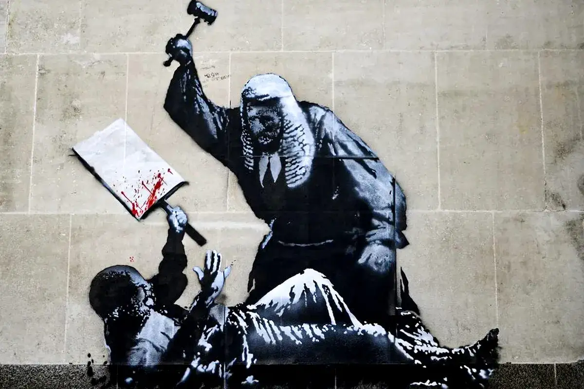 A judge in robes wields a gavel over a fallen figure holding a bloody sign. This is a classic Banksy piece, questioning justice.