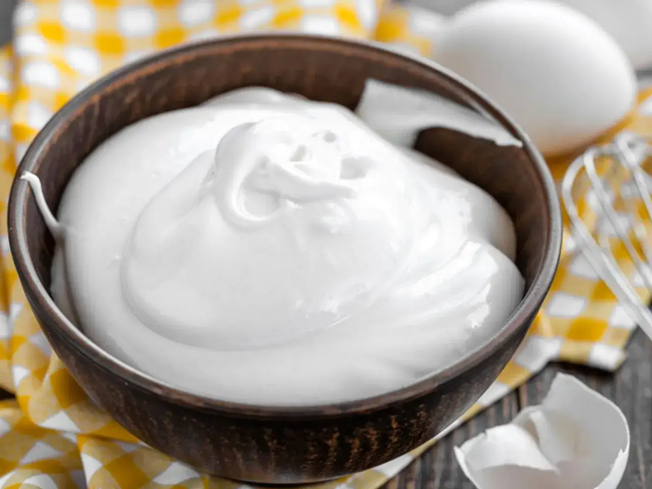 Sch&uuml;ssel mit cremigem Eischnee, der nicht fest wird. Daneben liegen Eierschalen und ein Schneebesen.
