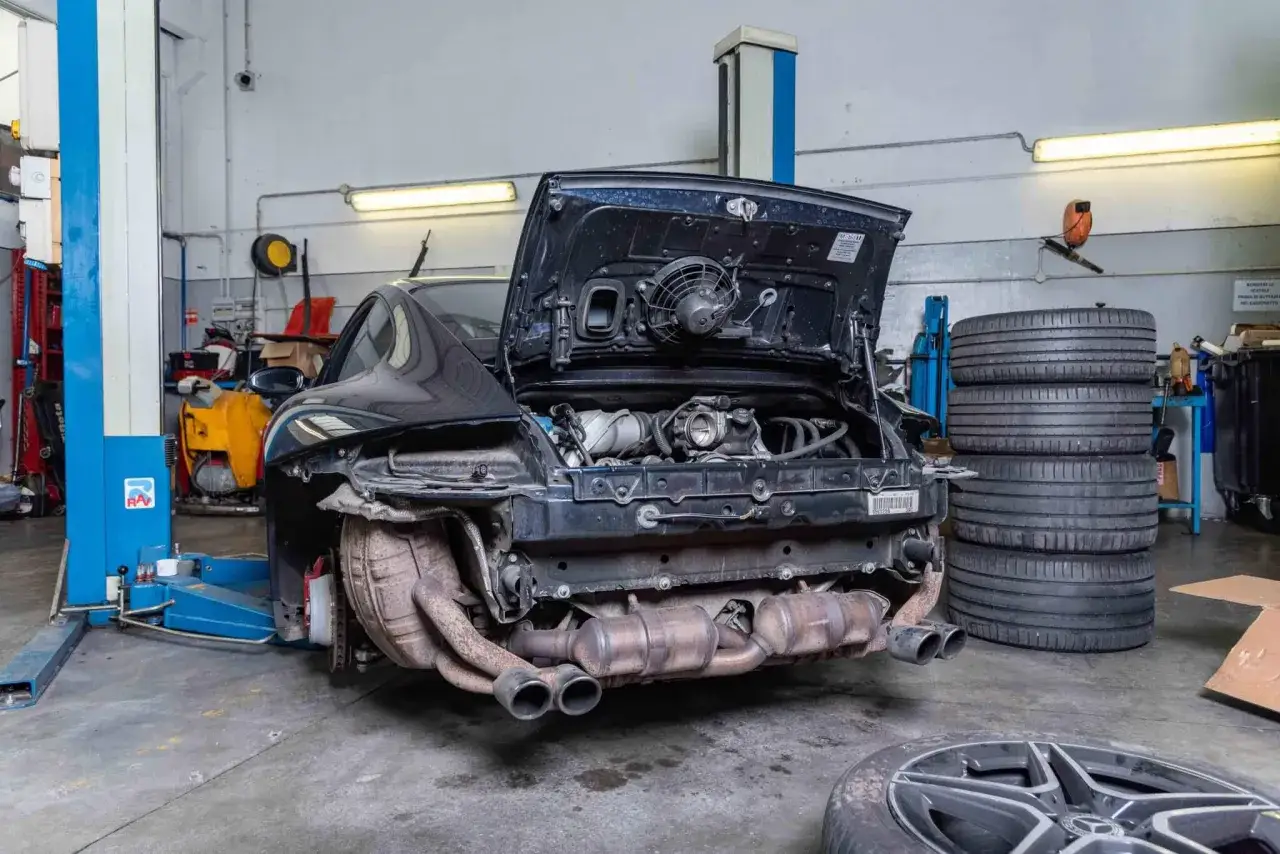 La carrozzeria della macchina è aperta, rivelando il motore e il sistema di scarico in un'officina.