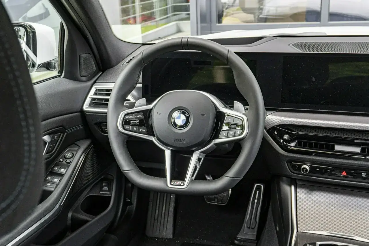Wnętrze BMW 330i G20. Skórzana kierownica z przyciskami, cyfrowe zegary i ekran multimediów.