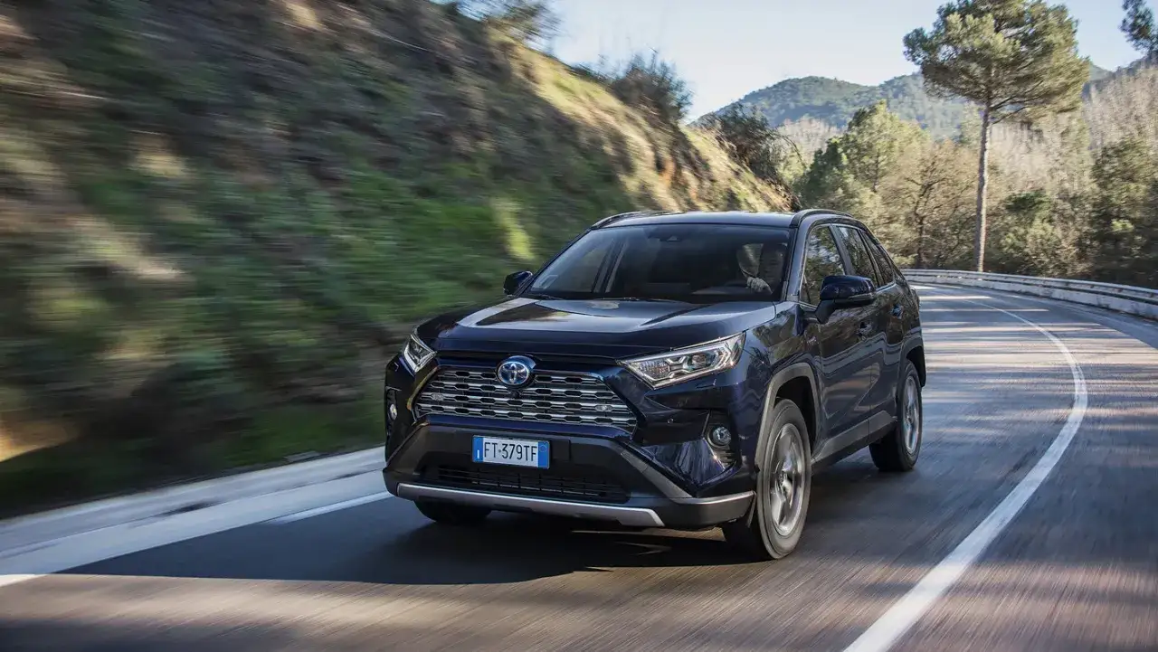 Ciemnoniebieski Toyota RAV4 Hybrid na krętej drodze w górach. Niskie spalanie to jego atut.