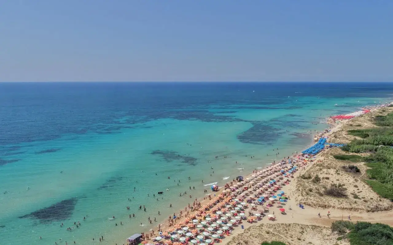 Spiaggia affollata con ombrelloni colorati e acque cristalline, le Maldive della Puglia dove si trovano per godersi il sole.