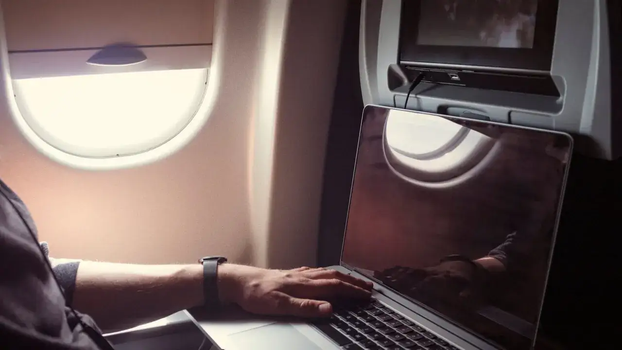 Praca na laptopie w samolocie. Czy w samolocie jest wifi? Widać ekran, okno i rękę na klawiaturze.