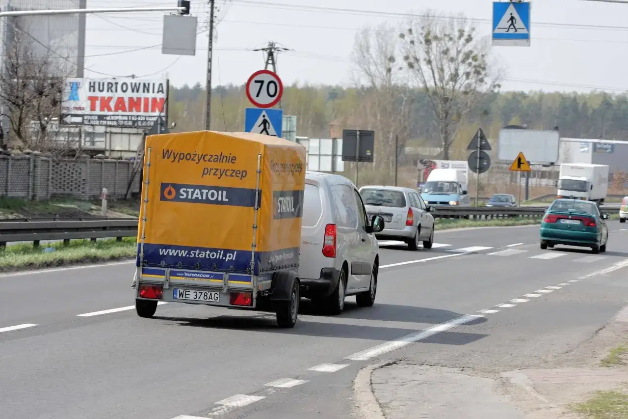 Samochód z żółtą przyczepką Statoil jedzie drogą. Znak ograniczenia prędkości do 70 km/h sugeruje, ile można jechać z przyczepką.