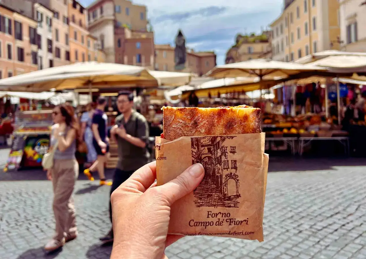Un pezzo di pizza appena sfornata, avvolto in carta con il logo 