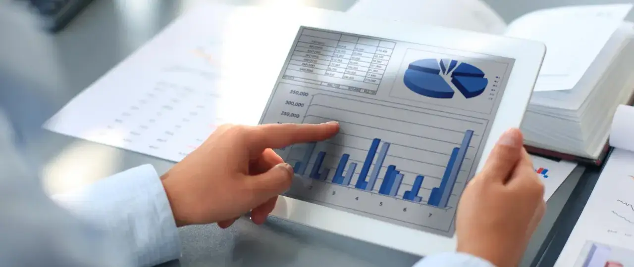 Ręka wskazuje na wykresy i tabelę na tablecie, analizując sprawozdanie finansowe.