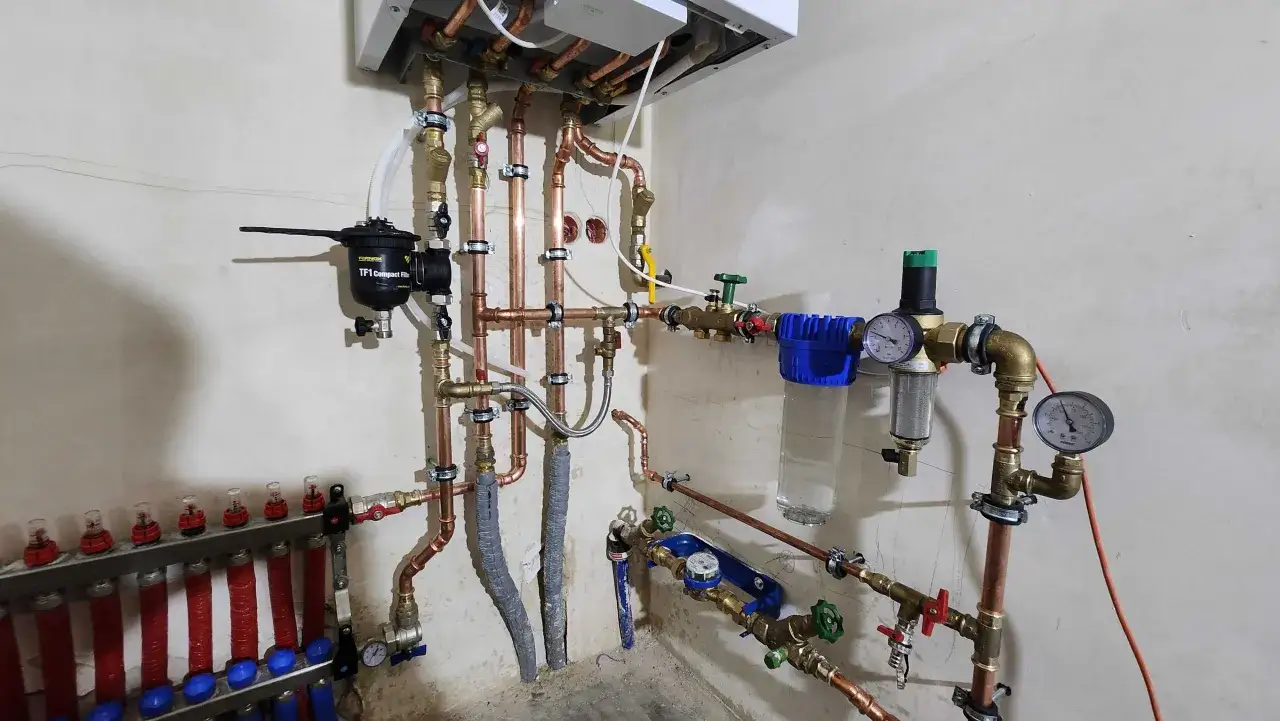 Profesjonalna instalacja cwu z miedzianymi rurami, filtrami i manometrami. System zapewnia ciepłą wodę użytkową.