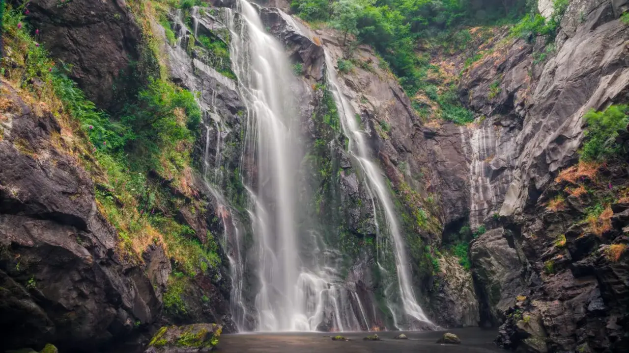 La Fervenza das Hortas, una cascada imponente que desciende por rocas cubiertas de vegetación exuberante, creando un paisaje natural de gran belleza.