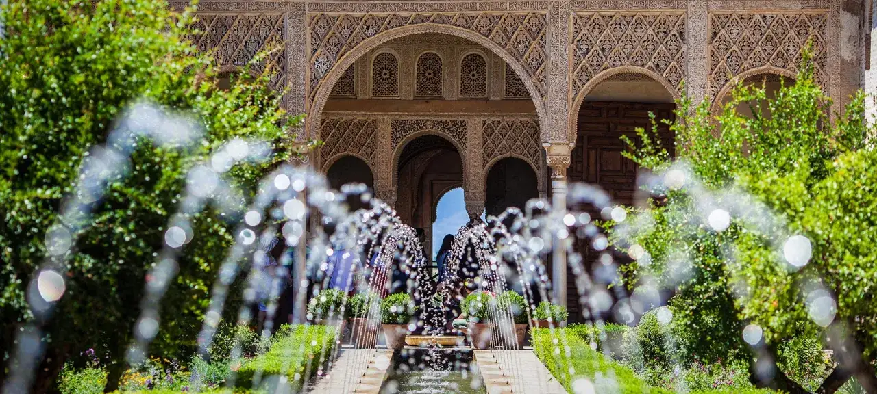 Plätschernde Brunnen im Generalife der Alhambra vor kunstvoll verzierten Bögen und üppigem Grün.