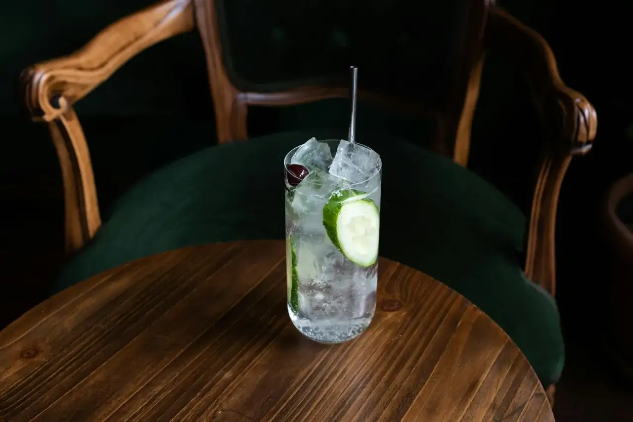 Przesłodzony drink? Jak uratować koktajl bitterem. Orzeźwiający napój z ogórkiem i wiśnią na drewnianym stoliku.