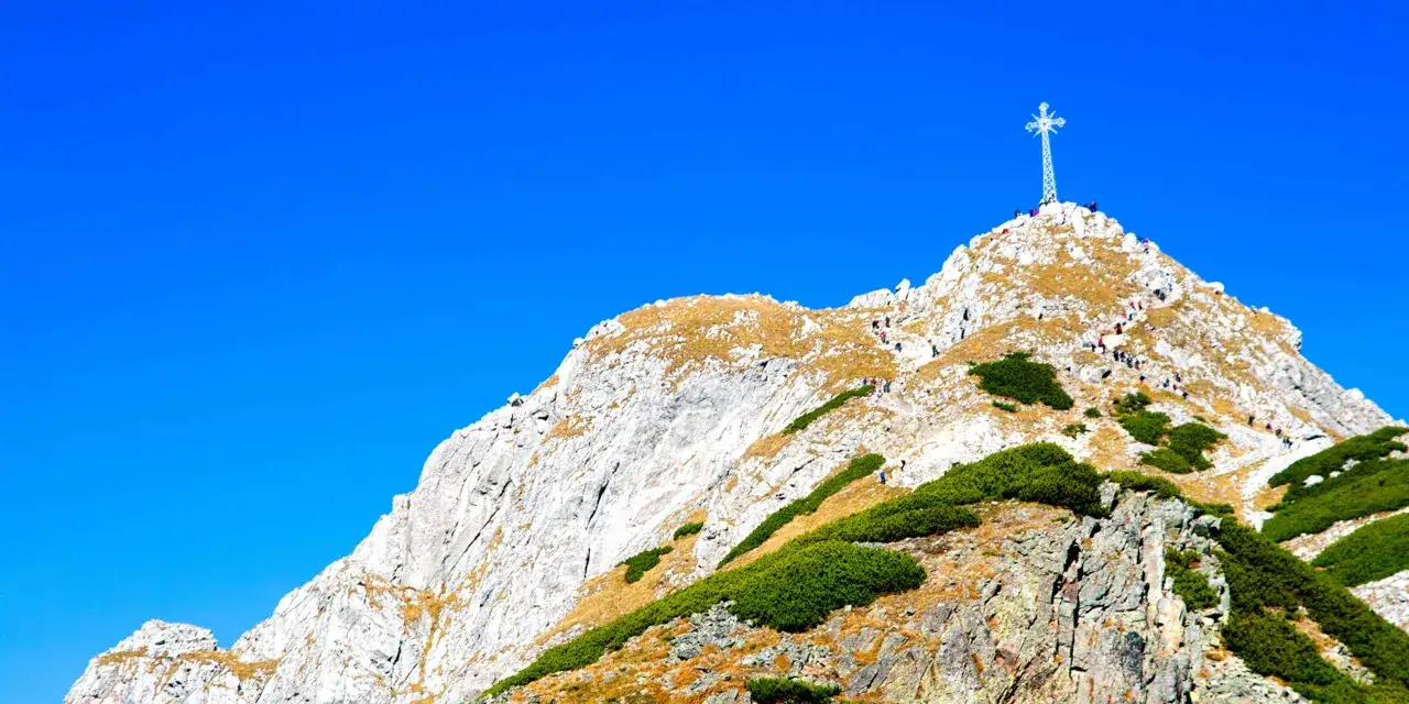 Giewont, symbol Tatr, wznosi się dumnie, a jego wysokość przyciąga turystów. Na szczycie widnieje krzyż.