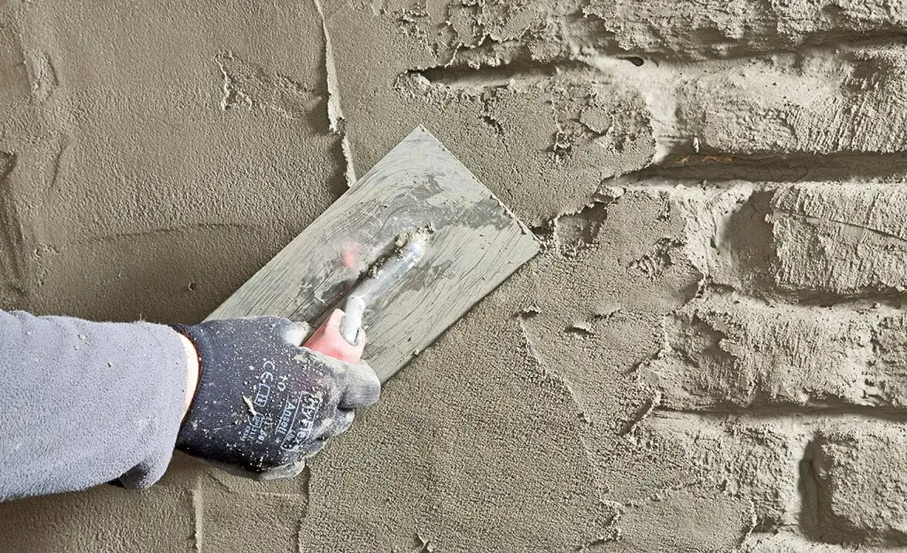 Hand mit Handschuh verputzt eine Wand. Dies ist ein wichtiger Schritt, um das Haus abzudichten und vor Feuchtigkeit zu schützen.