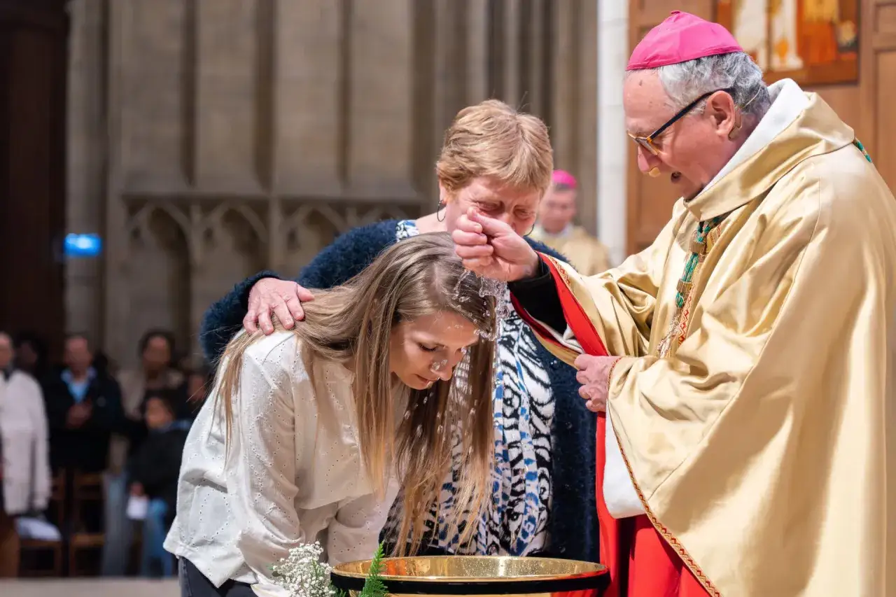 Un &eacute;v&ecirc;que verse de l'eau b&eacute;nite sur la t&ecirc;te d'une jeune femme lors d'un bapt&ecirc;me catholique.