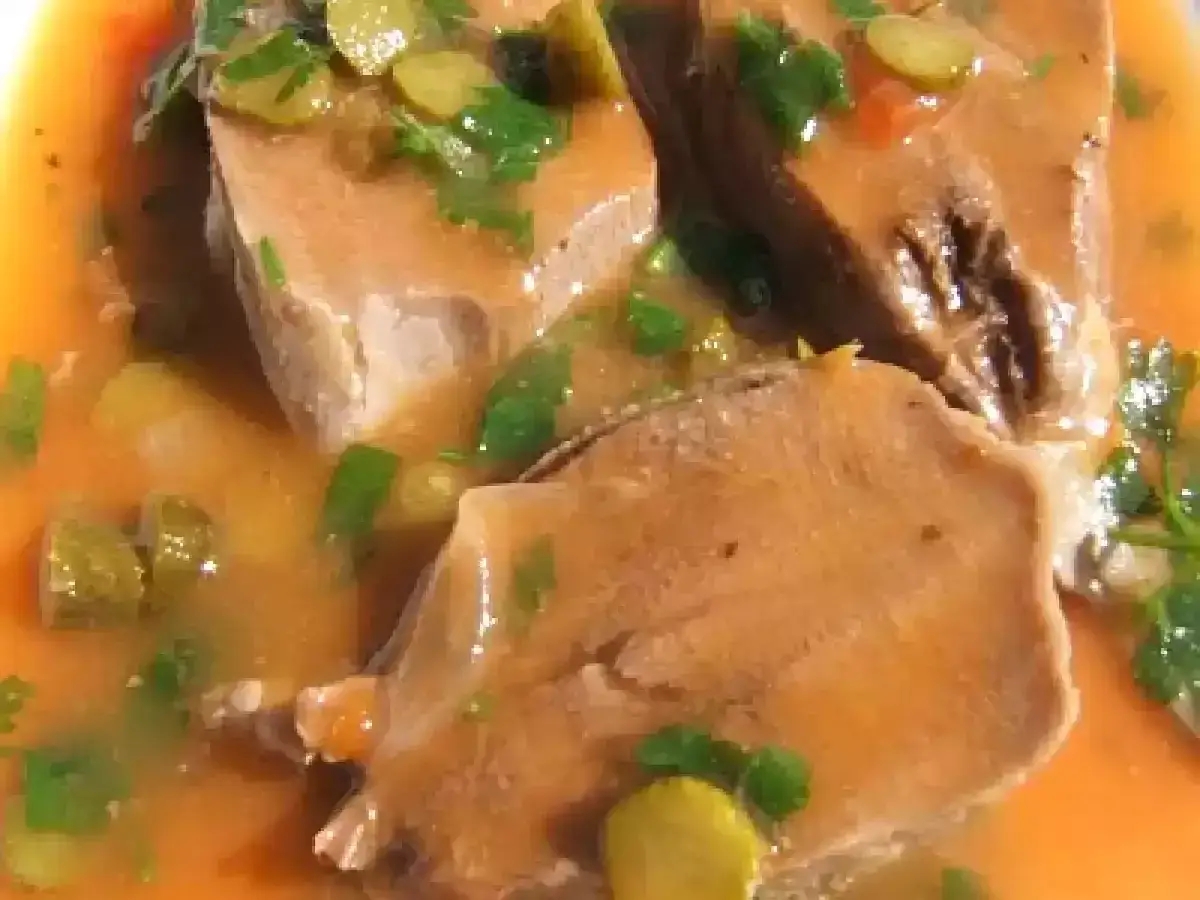 Tranches de langue de porc mijotées dans une sauce orangée, garnies de persil et de cornichons.